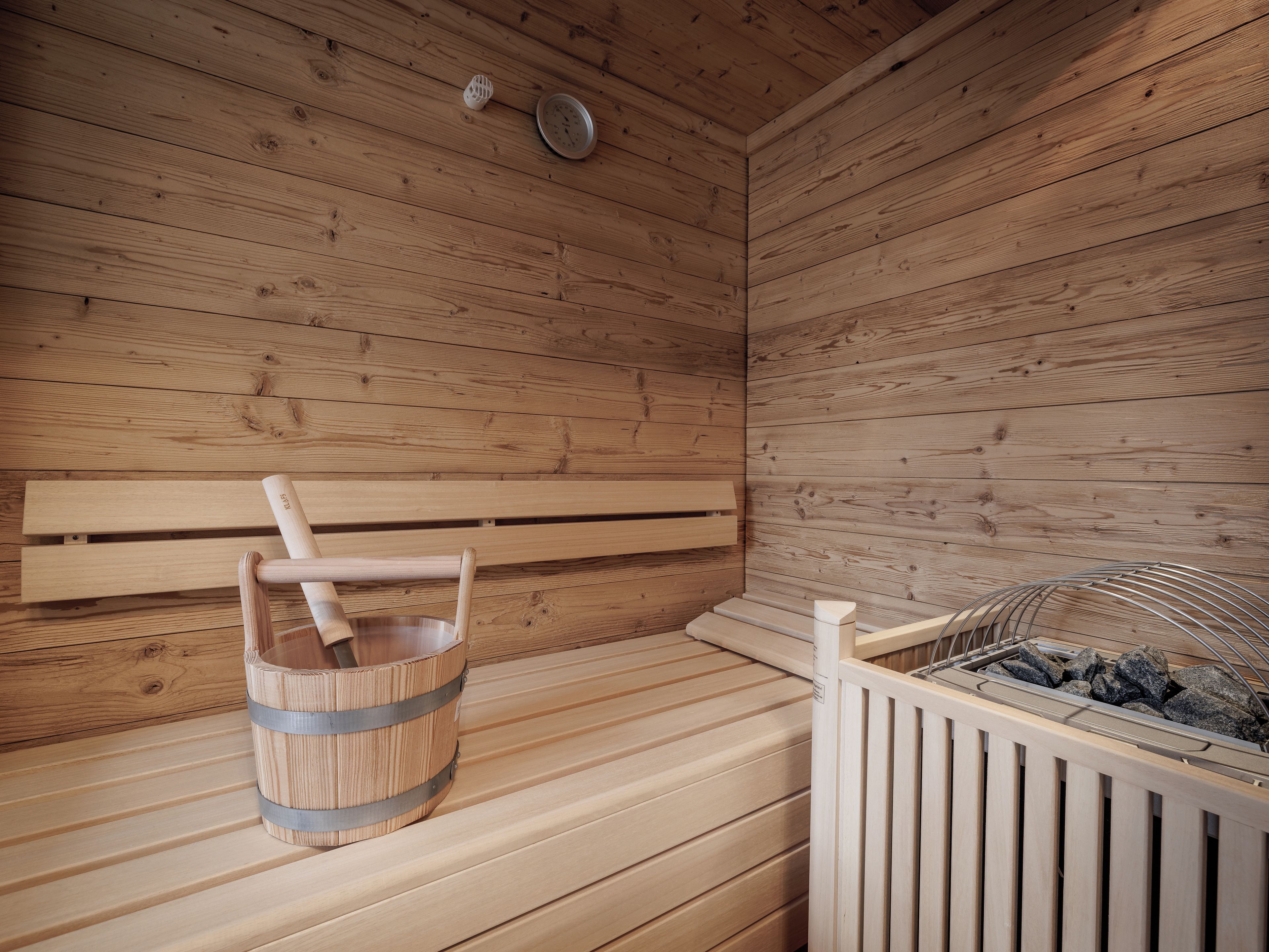 Una sauna de madera con bancos, un balde y un estante metálico con piedras.