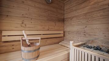 Una sauna de madera con bancos, un balde y un estante metálico con piedras.