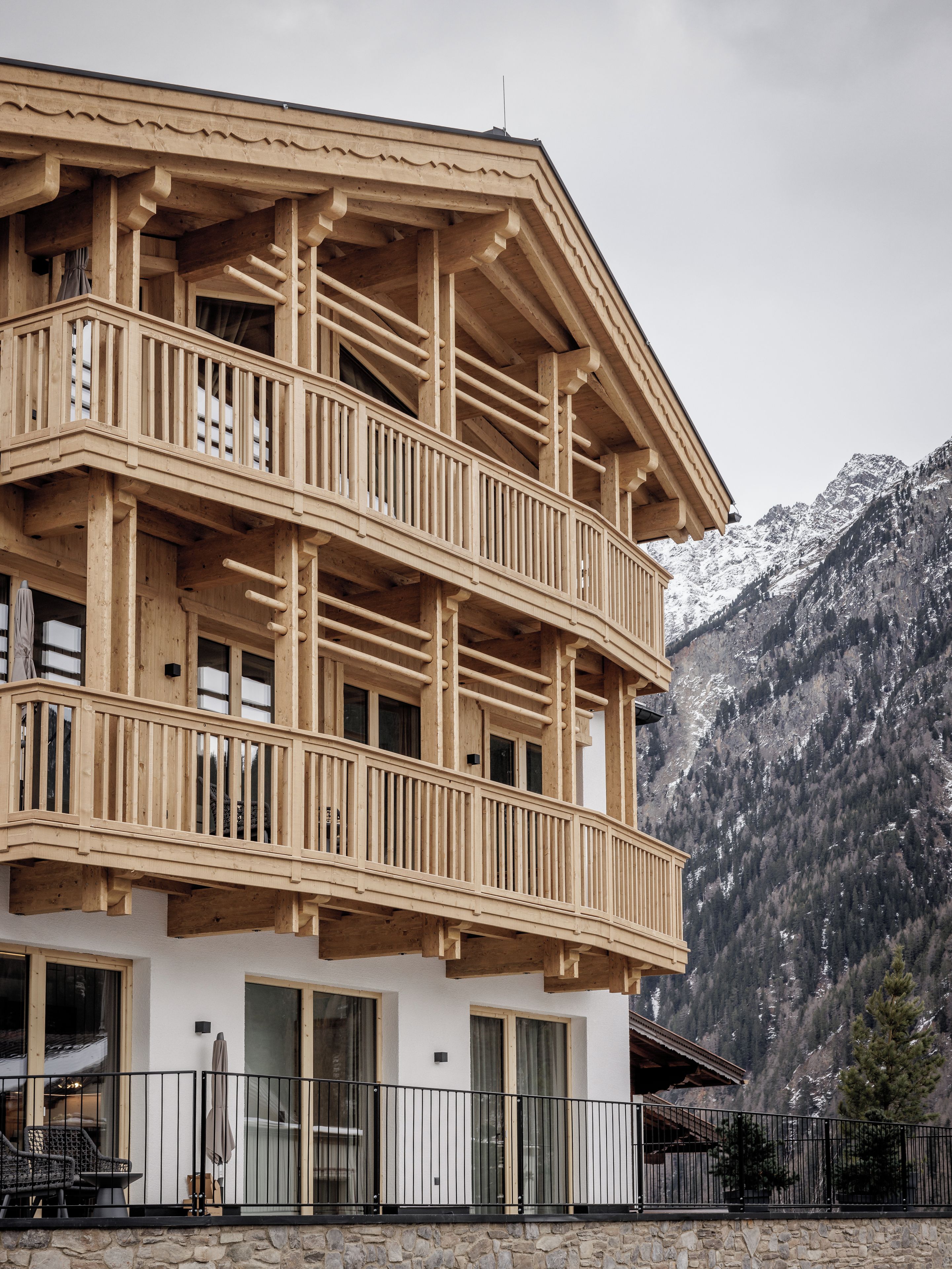 Ein mehrstöckiges Holzhaus mit Balkonen, einem Steinfundament und einer Bergkulisse.