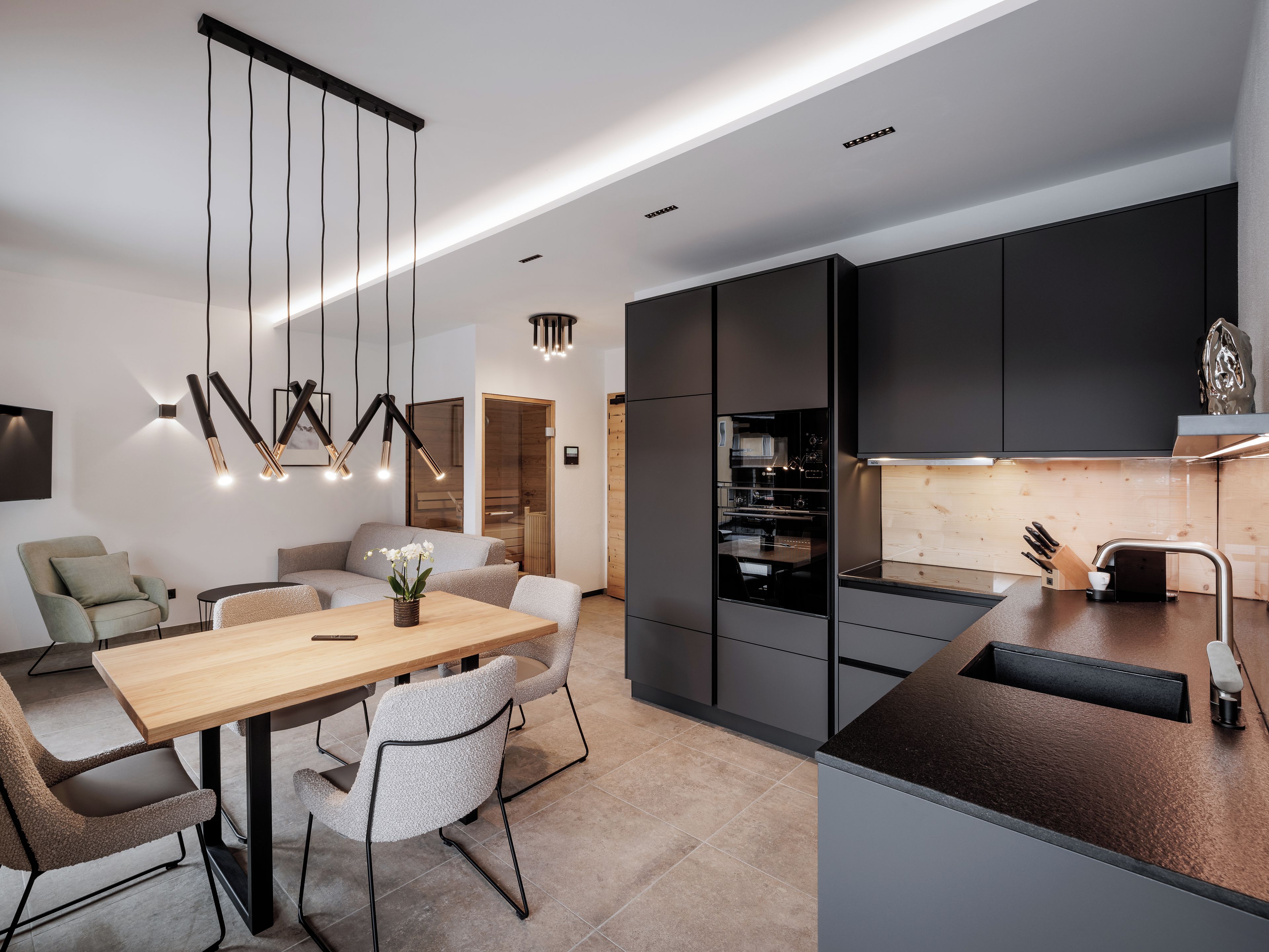 Una cocina moderna con armarios oscuros, una mesa de comedor de madera y un horno empotrado.
