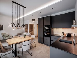 A modern kitchen with dark cabinetry, a wooden dining table, and a built-in oven.