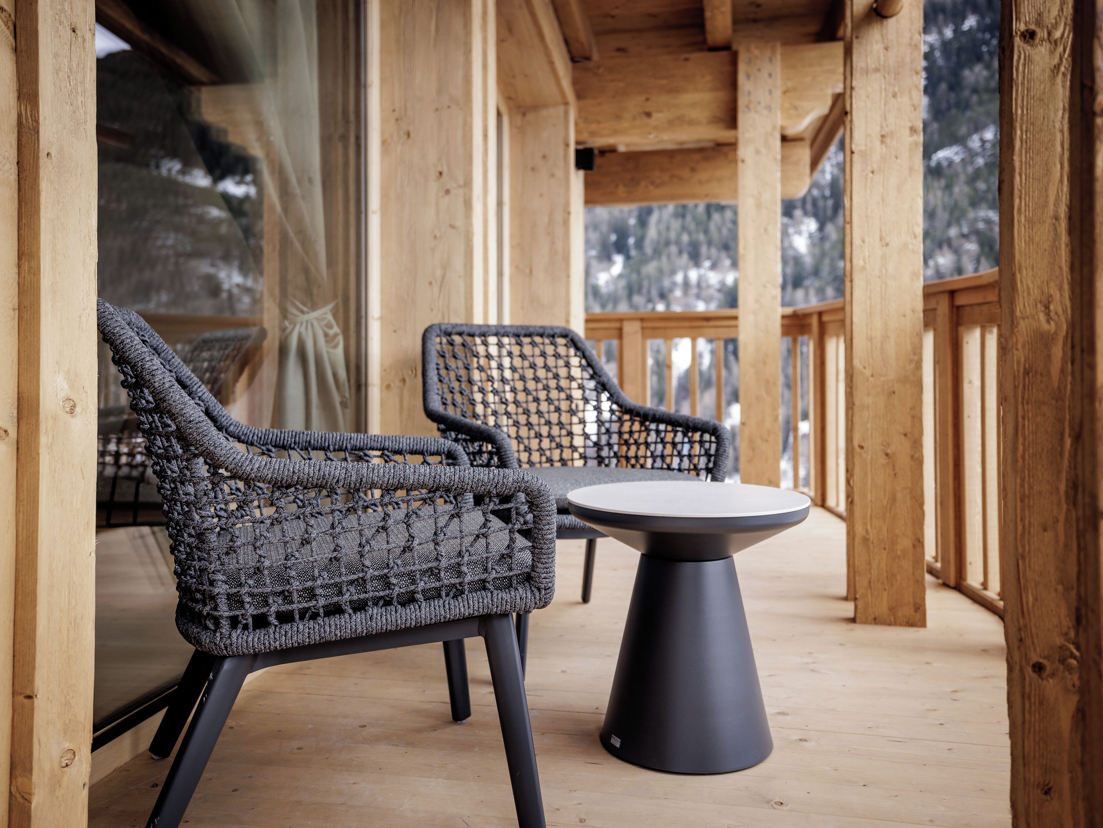 A wooden deck with two wicker chairs and a table.