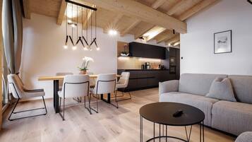 A modern living room with a wooden ceiling, a dining area with chairs and a table, and a kitchen in the background.