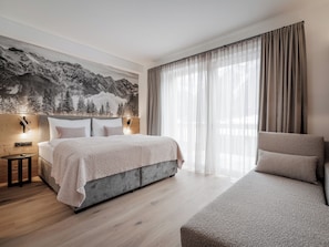 A modern bedroom with a bed, a nightstand, a wall-mounted lamp, a large window with curtains, and a mountain landscape mural.