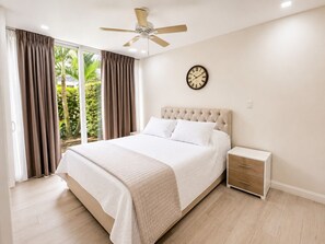 A bedroom with a bed, a nightstand, a ceiling fan, a clock, and a view of greenery outside. - 1 Condominio en Herradura, Cerca Jacó y Los Sueños (Herradura)