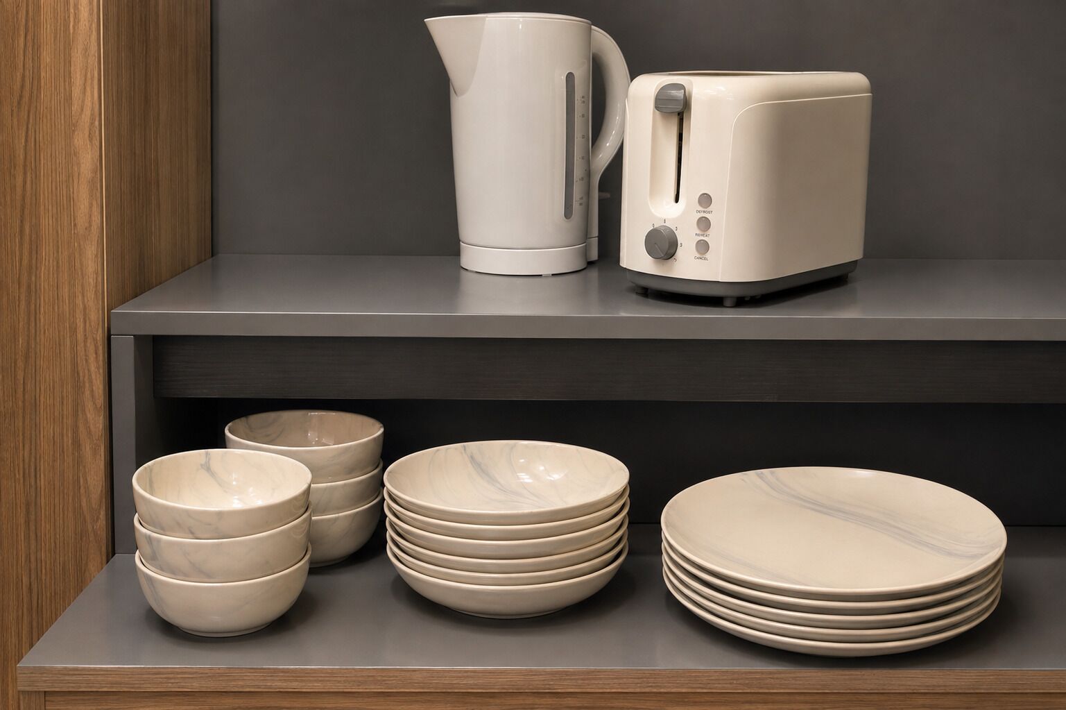 A kitchen area with a modern design, featuring a kettle, toaster, and various bowls and plates on a shelf.
