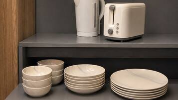 A kitchen area with a modern design, featuring a kettle, toaster, and various bowls and plates on a shelf.