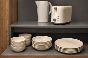 Ein Küchenbereich mit modernem Design, mit Wasserkocher, Toaster und verschiedenen Schüsseln und Tellern auf einem Regal.