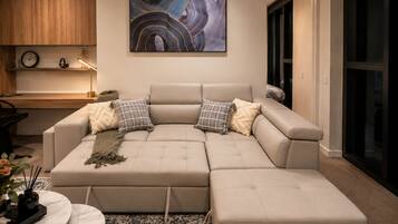 A modern living room with a sectional sofa, a large abstract painting, and a small wooden table with a clock and decorative items.
