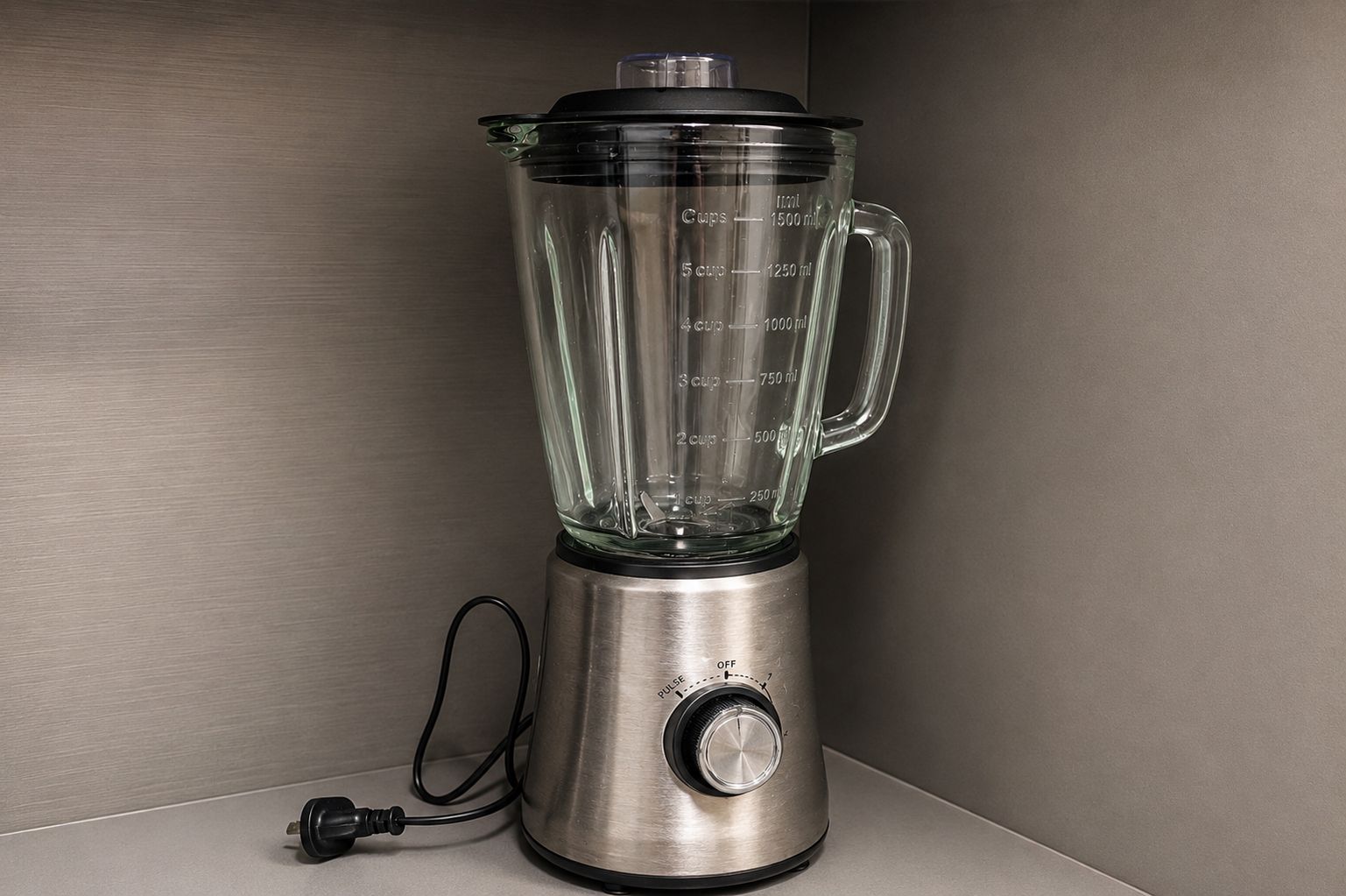 A stainless steel blender with a measurement scale, a power cord, and a black handle.