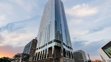 Un rascacielos alto y moderno con un diseño angular distintivo, rodeado de otros edificios y una calle con automóviles.