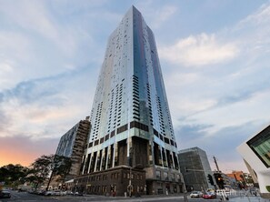 A tall, modern skyscraper with a unique angular design, surrounded by other buildings and a street with cars.
