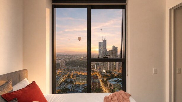 Une chambre avec une grande fenêtre donnant sur un paysage urbain au coucher du soleil.