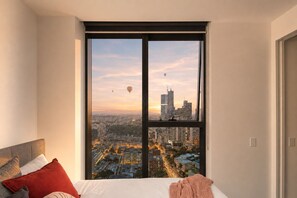 A bedroom with a large window overlooking a cityscape at sunset. - 19F Sky-Rise 2BR 2BTH, Panoramic CBD Views with Resort-Style Amenities (Carlton)