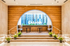 A modern interior with a wooden wall, a large arched window, and a seating area with two tables and chairs.