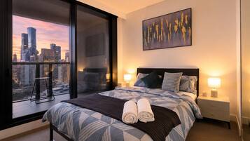 A hotel room with a large bed, two bedside tables, a city view, and a painting on the wall.