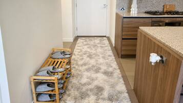Un pasillo con un zapatero de madera, un felpudo mullido, una puerta blanca, armarios de madera y una encimera con un florero.