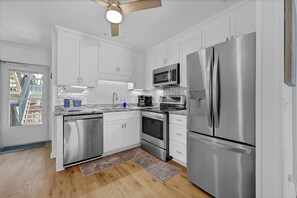 Una cocina moderna con electrodomésticos de acero inoxidable, armarios blancos y piso de madera.