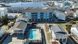 A coastal residential area with a large blue building, a swimming pool, and a marina in the background. - Beach Getaway | Updated 2BR Condo, Pool & Beach Access (Carolina Beach)