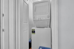 A laundry room with a stacked washer and dryer, a door, and a blue basket.
