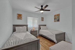 Une chambre avec deux lits, un ventilateur de plafond, une table de chevet avec une lampe et des œuvres d’art accrochées aux murs.