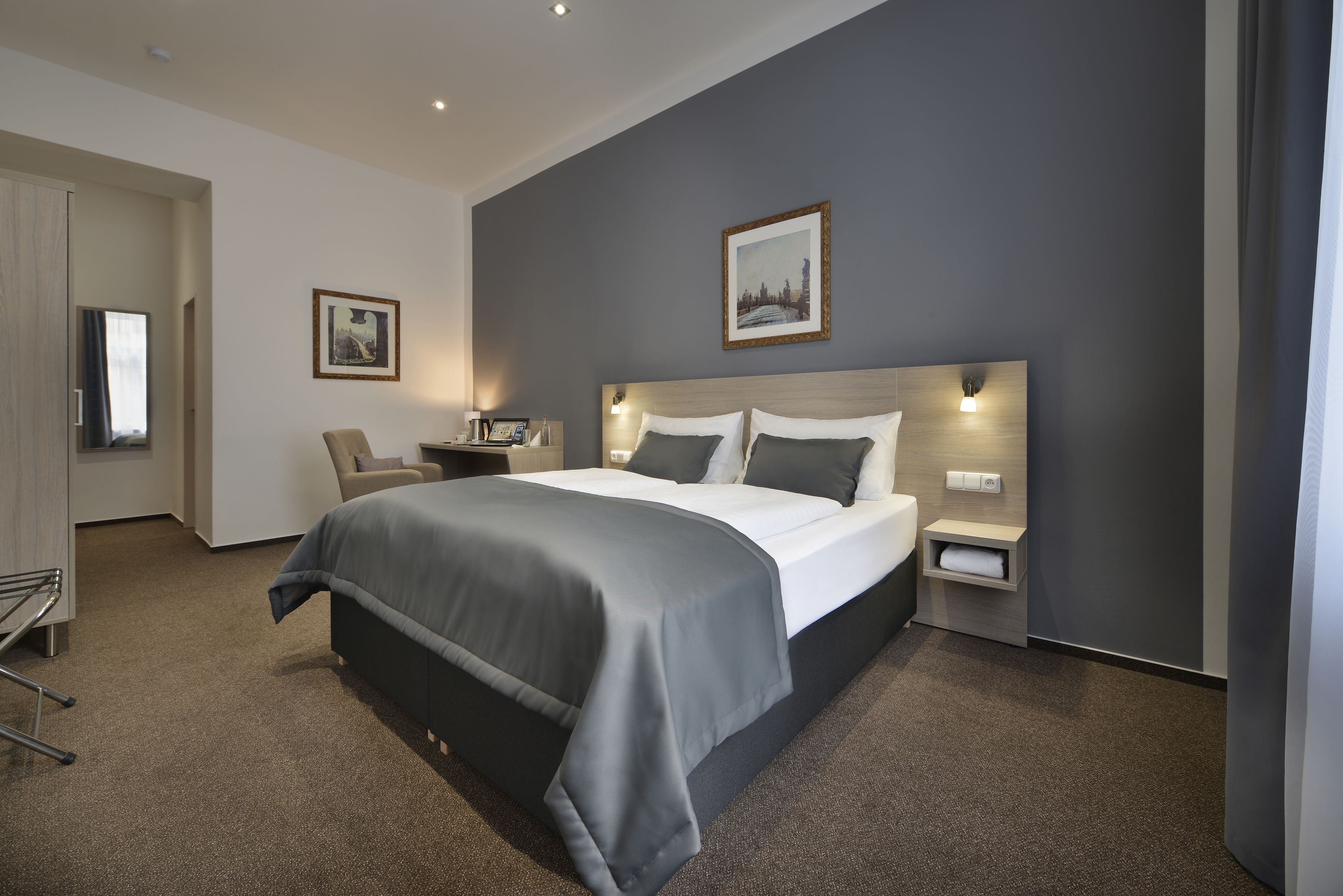 A modern hotel room with a large bed, bedside tables, a chair, and a desk.