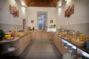 A well-lit kitchen with wooden cabinets, a central island with food items, and a view of the dining area through a glass door. - Prague Season Hotel (Prague)