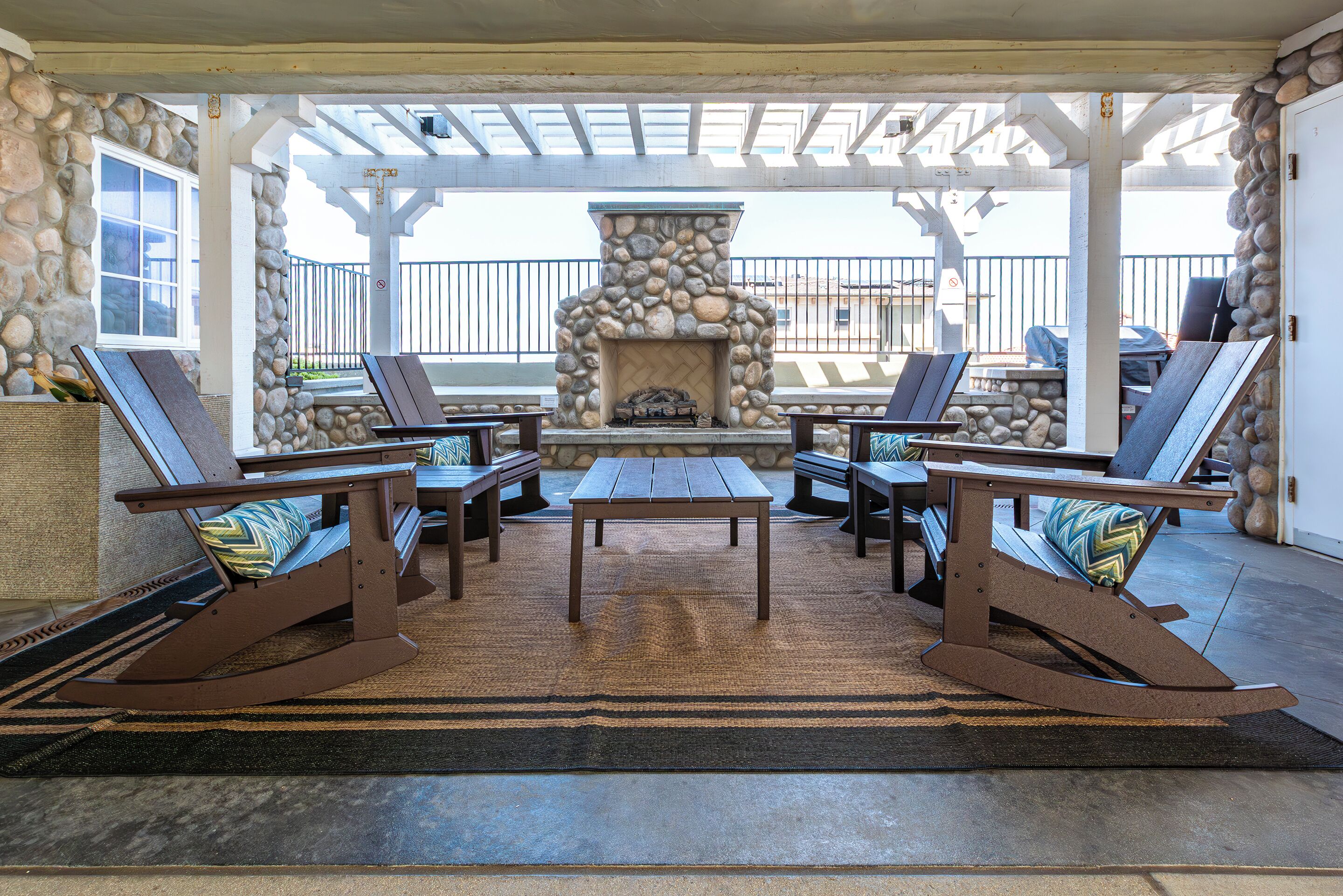 A covered patio with a stone fireplace, lounge chairs, and a table.