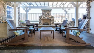 A covered patio with a stone fireplace, lounge chairs, and a table.