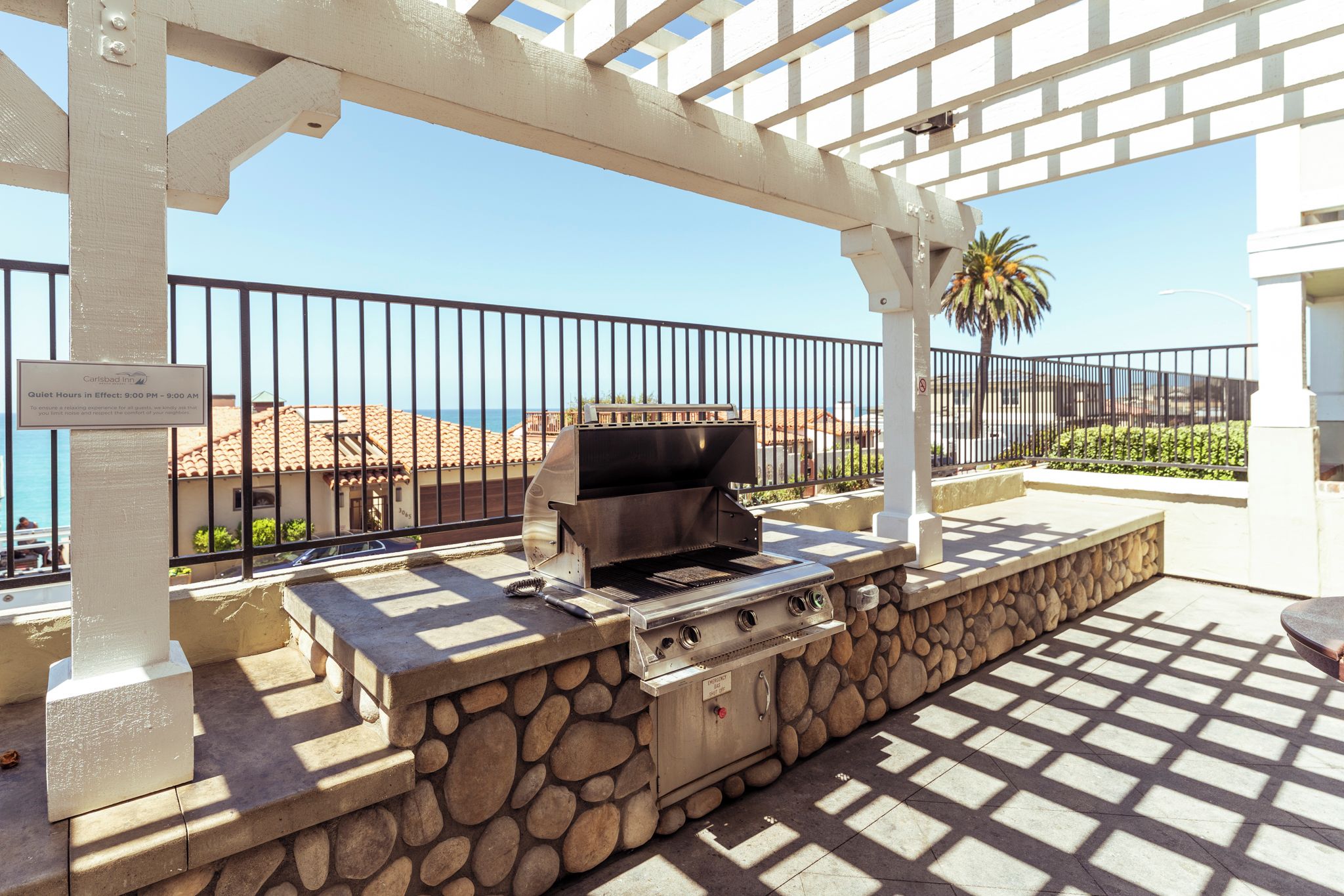 An outdoor grill area with a stone base, a metal grill, and a pergola structure.