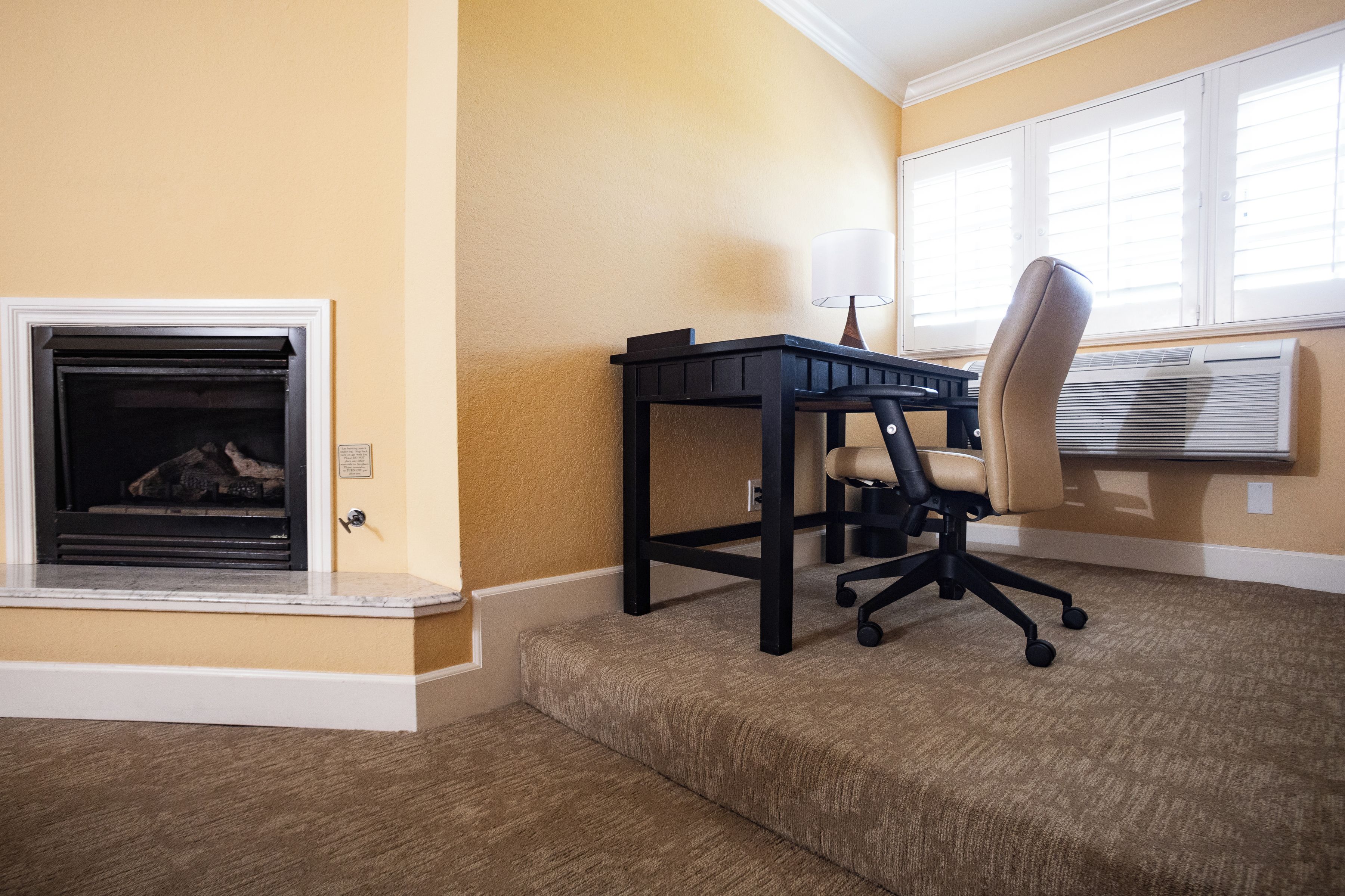 A room with a fireplace, a desk with a chair, and an air conditioning unit.