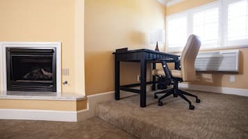 A room with a fireplace, a desk with a chair, and an air conditioning unit.