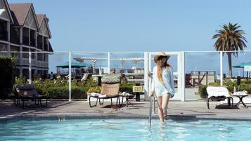 Zona de piscina con sillones de descanso y sombrillas, cielo despejado y un edificio al fondo.