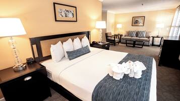 A hotel room with a large bed, two bedside tables, a nightstand, a sofa, a chair, and a desk.