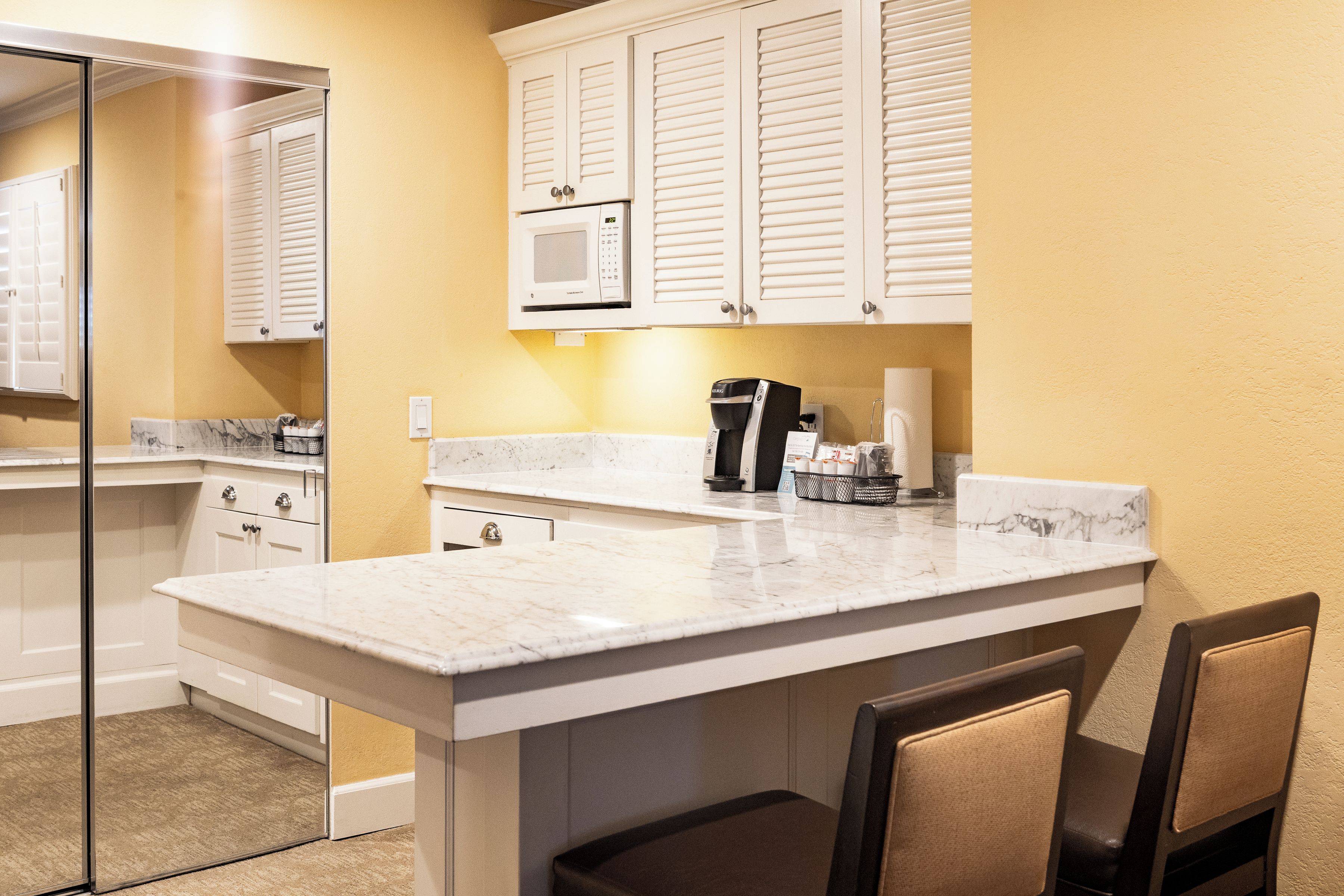 A compact kitchen with a marble countertop, white cabinets, and a coffee machine.