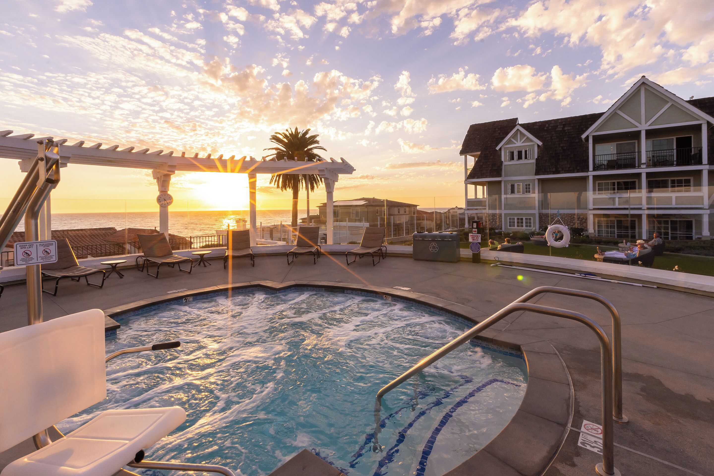 A pool area with lounge chairs and a pergola during sunset.