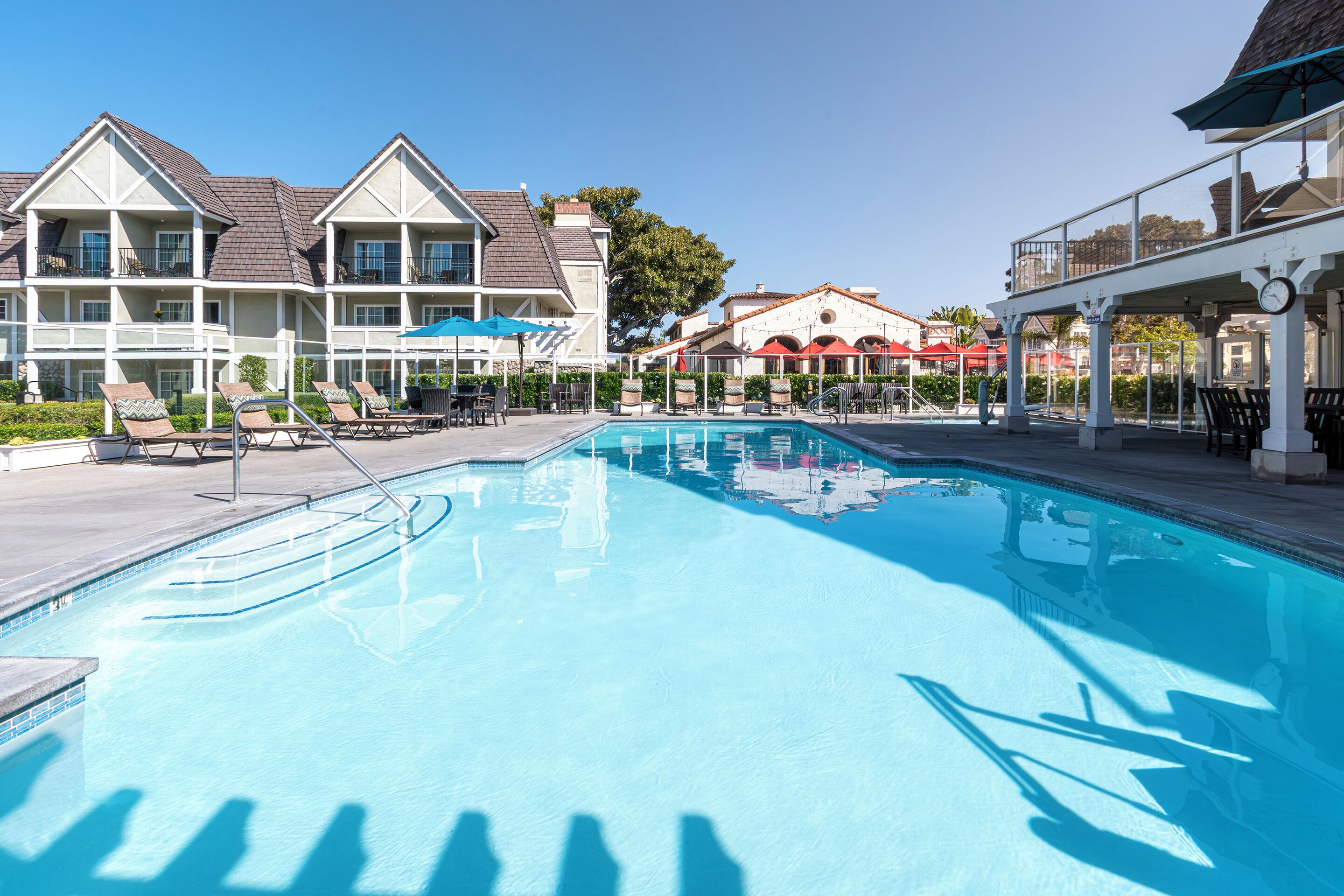 A swimming pool with lounge chairs and umbrellas, surrounded by buildings with balconies and a clear sky.