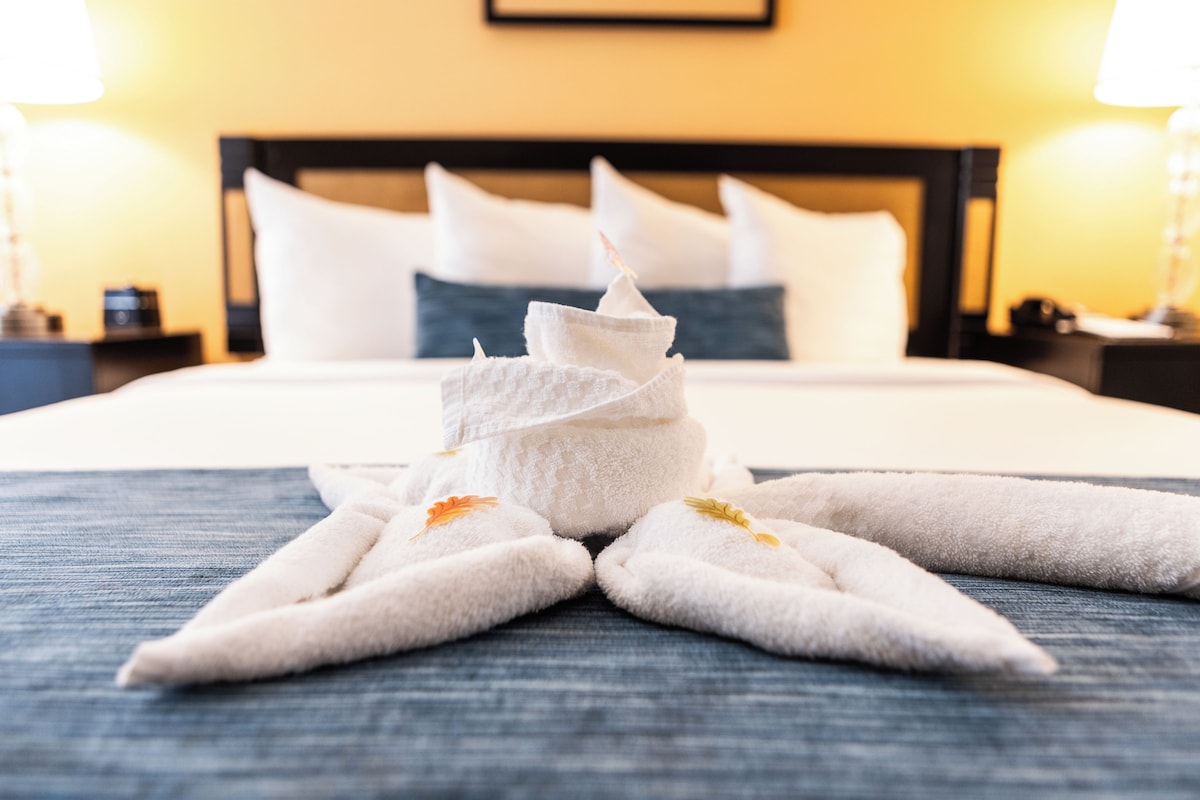 A neatly made bed with a towel arrangement in the shape of a star, a headboard, and a bedside table with a lamp.