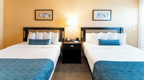 A hotel room with two beds, a nightstand, a lamp, and artwork on the walls. - Carlsbad Inn Beach Resort Hotel (Carlsbad)