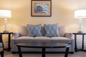 Ein Wohnzimmer mit einer Couch, zwei gemusterten Kissen, einem Couchtisch und je einer Lampe auf jeder Seite.