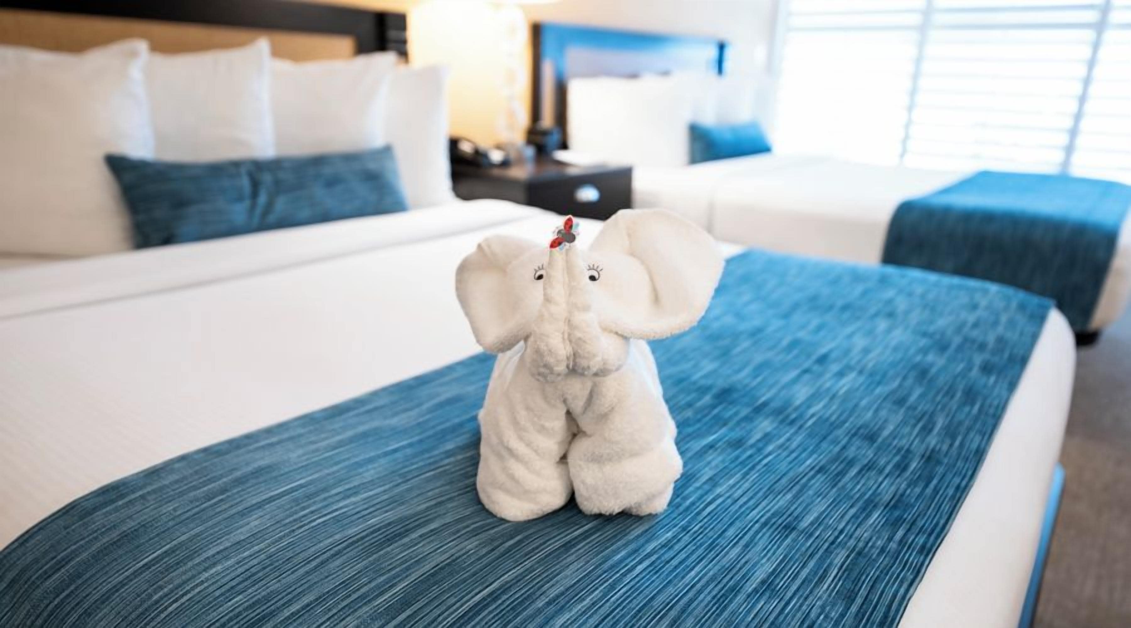 A bed with a blue bedspread, a white headboard, and a plush elephant toy on the bed.