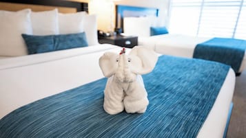 A bed with a blue bedspread, a white headboard, and a plush elephant toy on the bed.