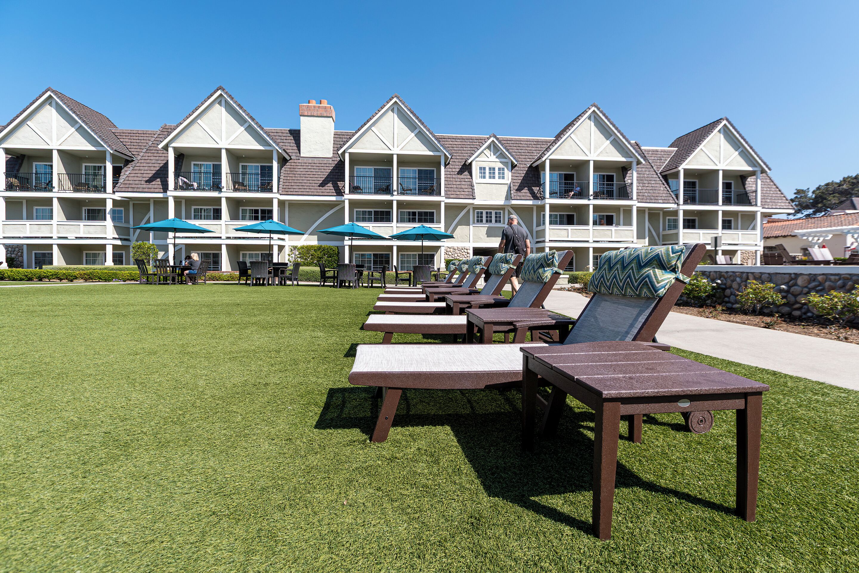 A hotel with multiple balconies, outdoor seating with umbrellas, and a well-maintained lawn.