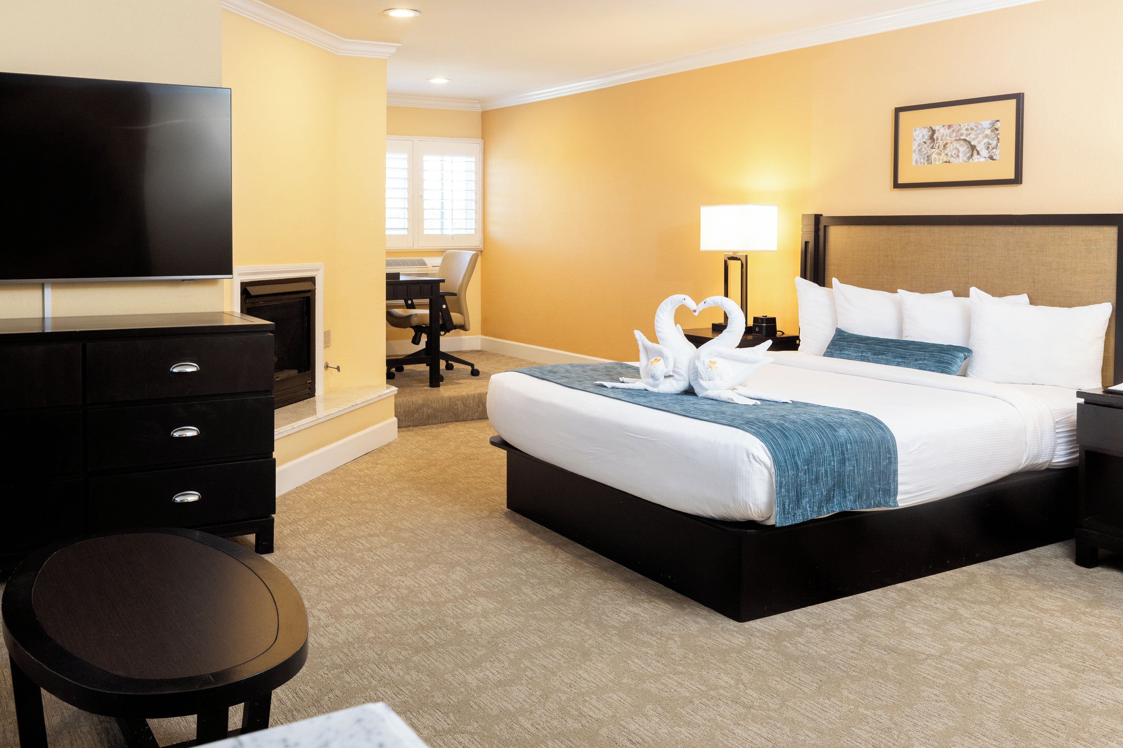 A hotel room with a bed, a desk, a chair, a TV, and a lamp.