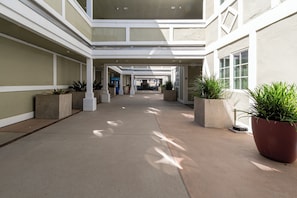 A covered corridor with concrete flooring, potted plants, and a central seating area.