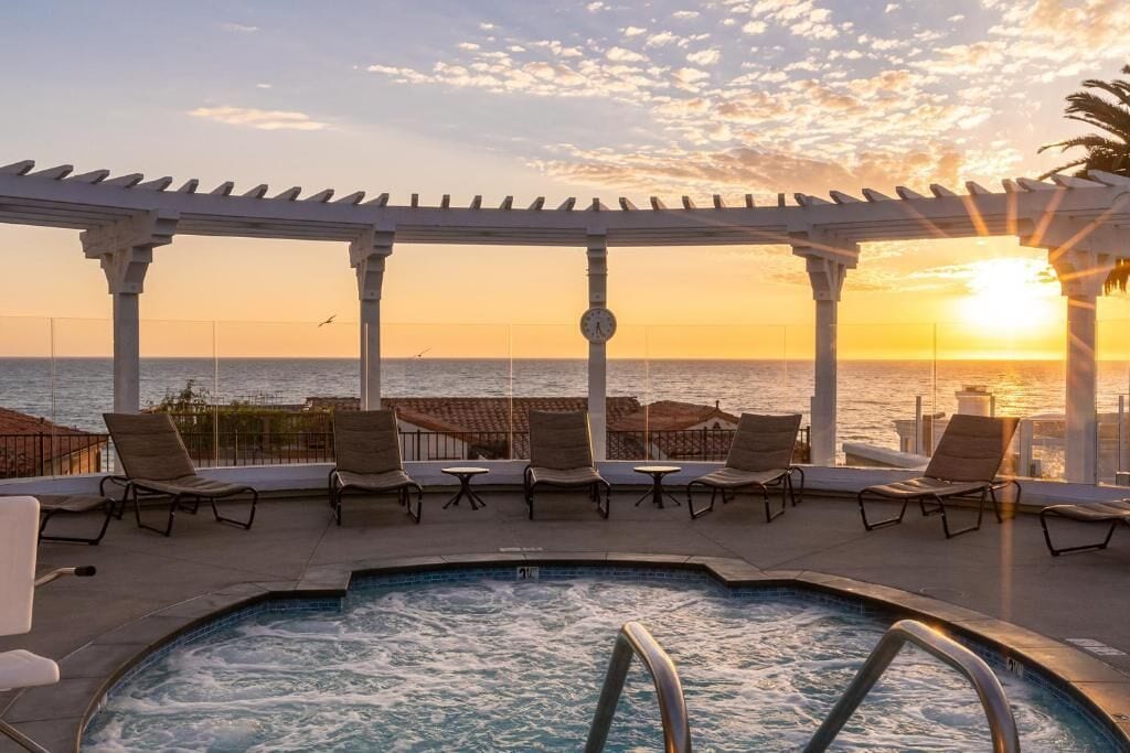 A pool area with lounge chairs and a pergola overlooking the sea during sunset.