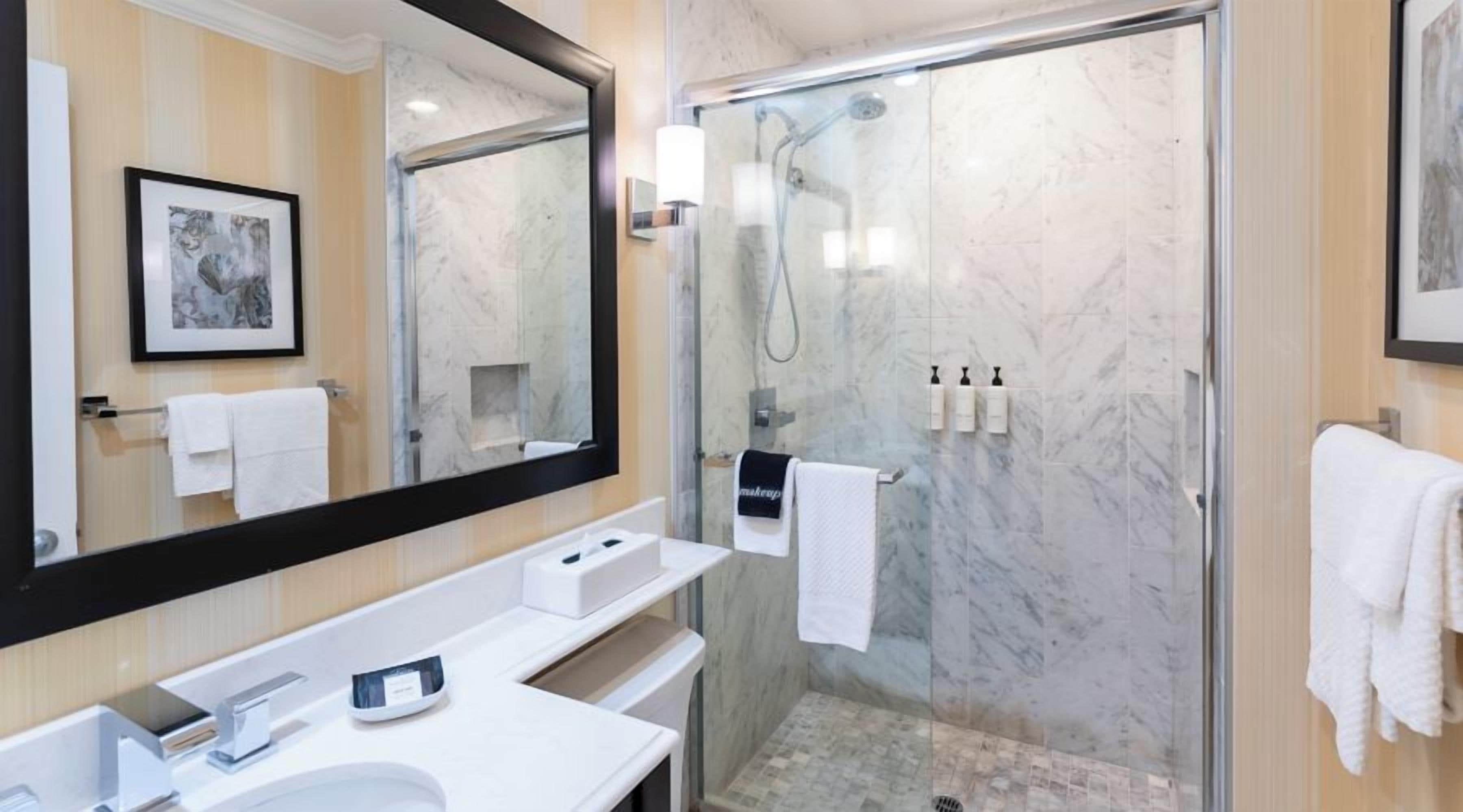 Un baño moderno con ducha envuelta en vidrio, un espejo grande y un lavamanos blanco.