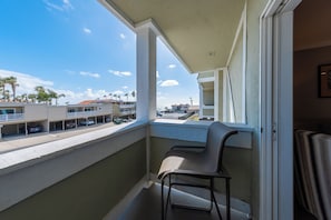A balcony with a chair, a view of the street, and a building with a balcony.