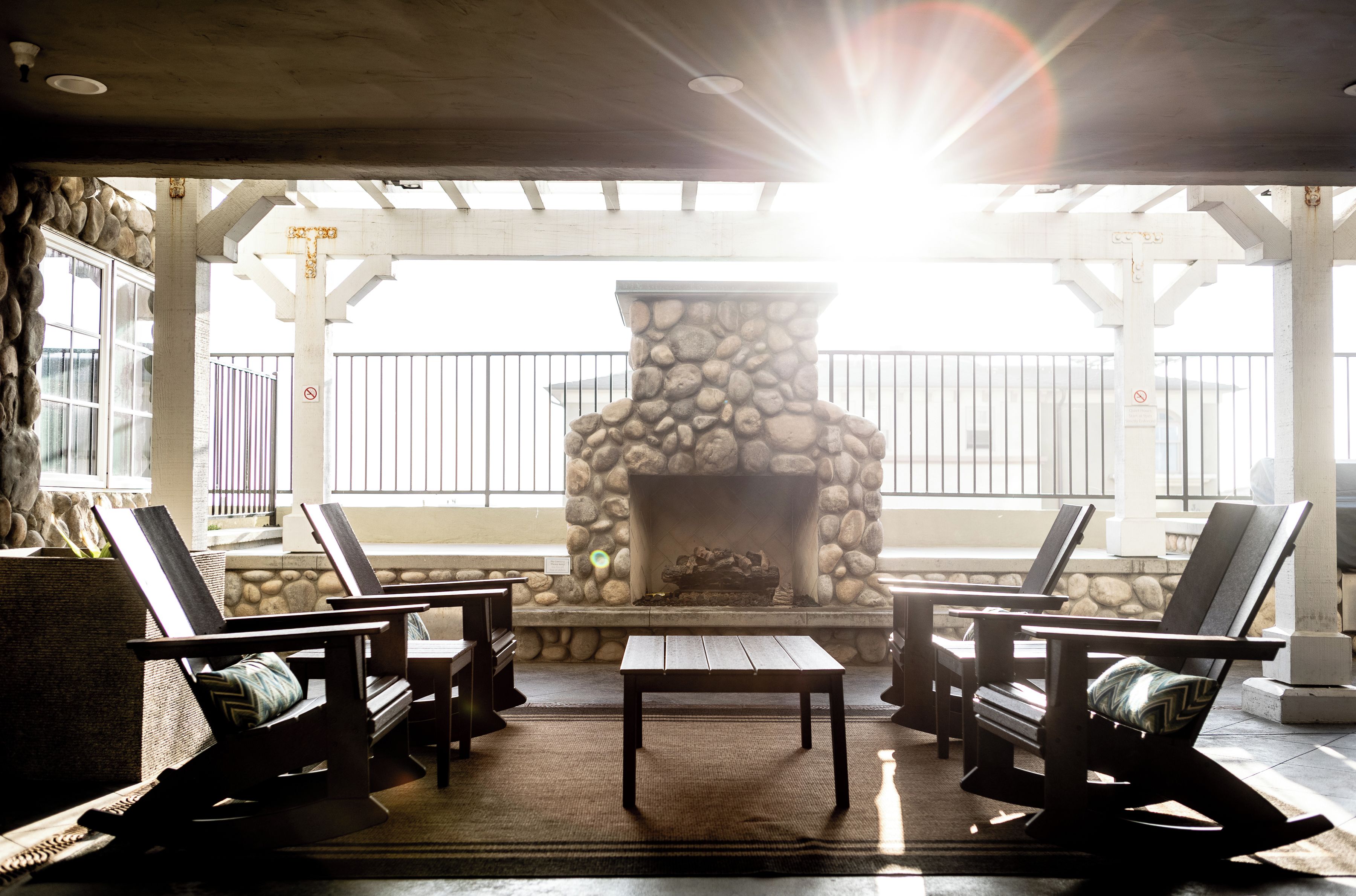 An outdoor seating area with a stone fireplace, wooden chairs, and a view of the ocean.