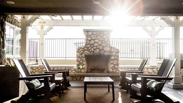 An outdoor seating area with a stone fireplace, wooden chairs, and a view of the ocean.